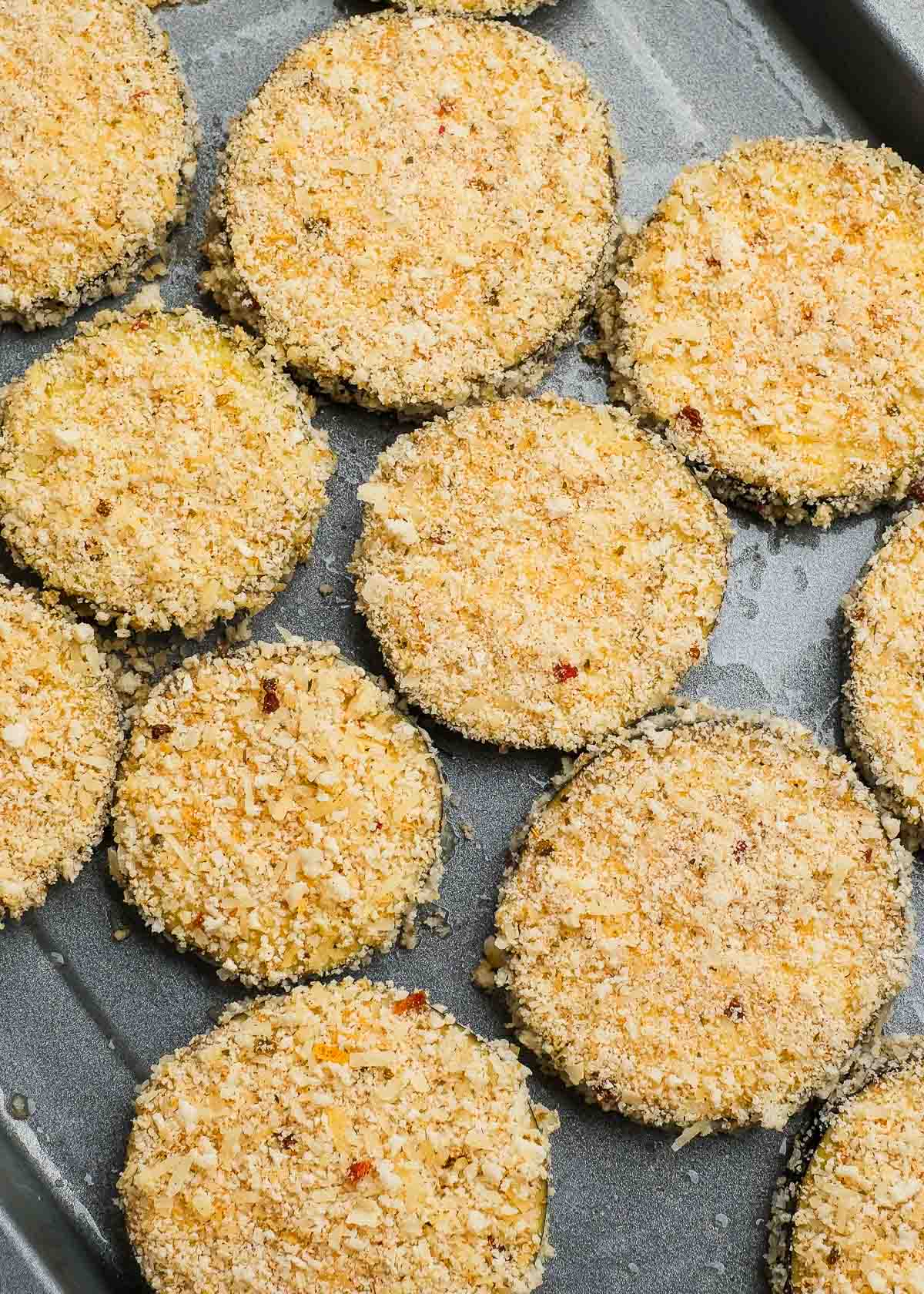 several zucchini rounds covered in seasoned breading and placed on a greased baking sheet