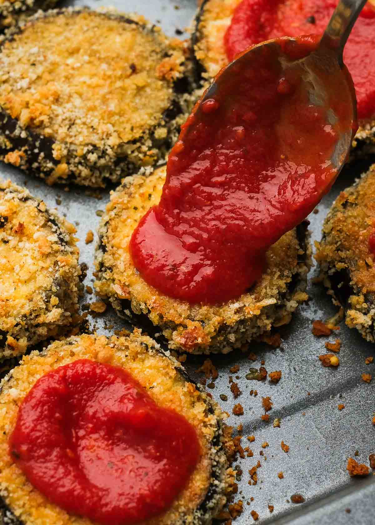 spooning marinara sauce onto crispy breading to make zucchini parmesan