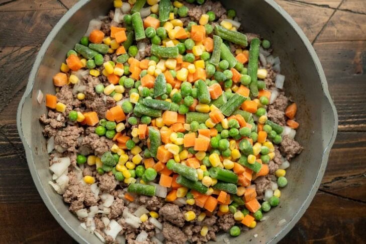 browned ground beef in a skillet with frozen mixed vegetables
