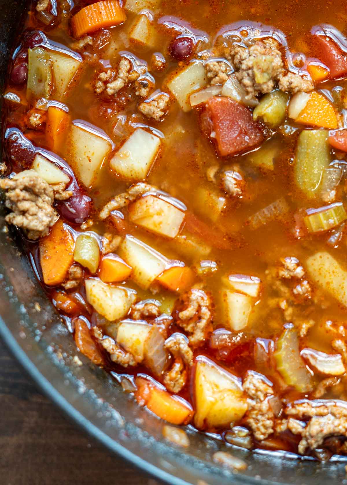 a brothy soup filled with potatoes, ground beef, green beans, tomatoes, carrots, onions, garlic, and celery