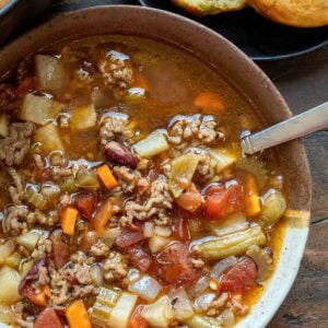 a bowl filled with hearty cowboy soup beside a plate full of cornbread