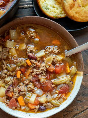 a bowl filled with hearty cowboy soup beside a plate full of cornbread