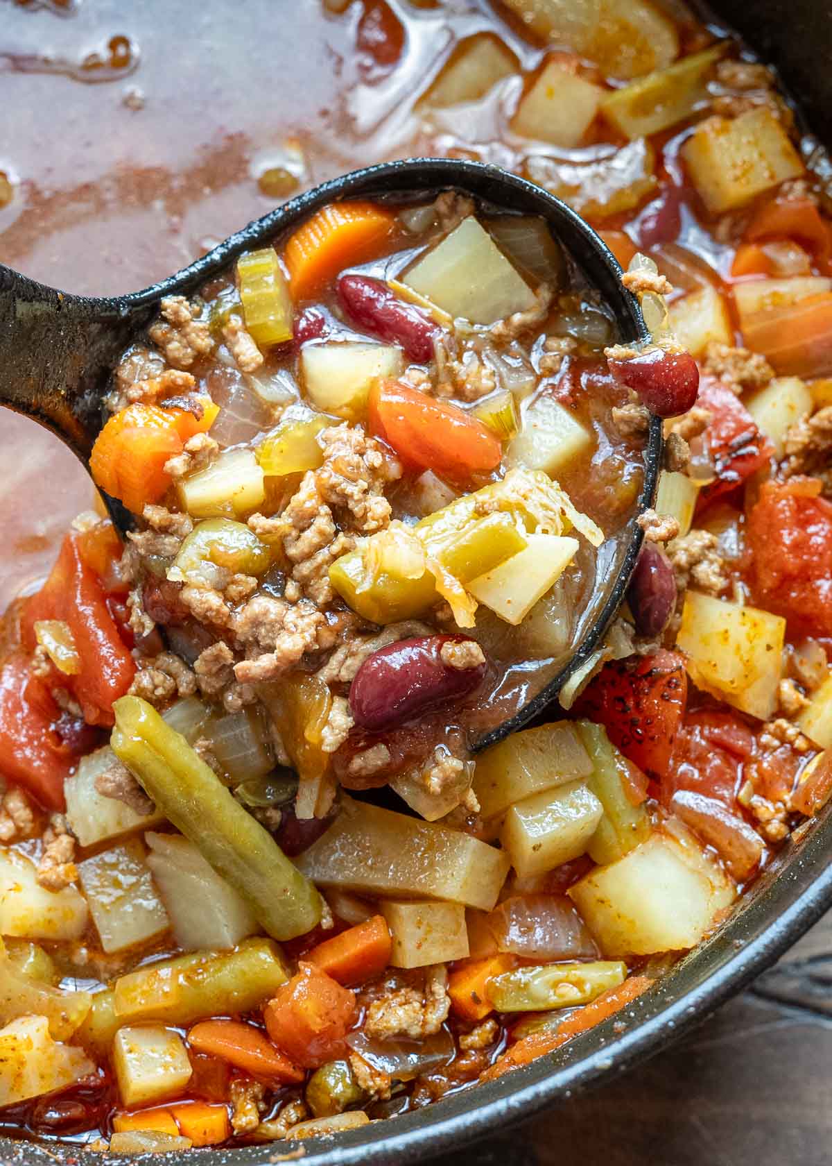 a ladle filled with beef and veggies in a pot of cowboy soup