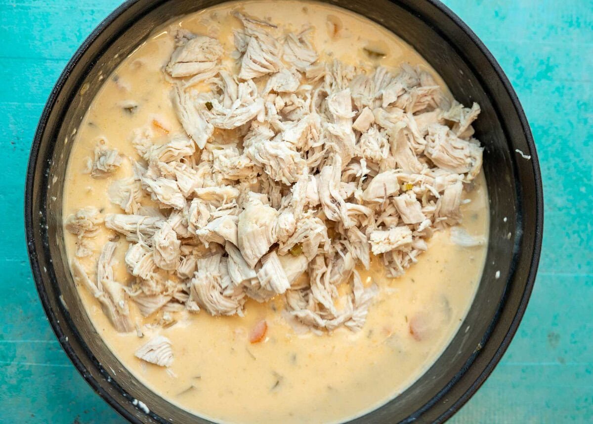 shredded chicken atop a creamy gluten-free soup base in a large black pot