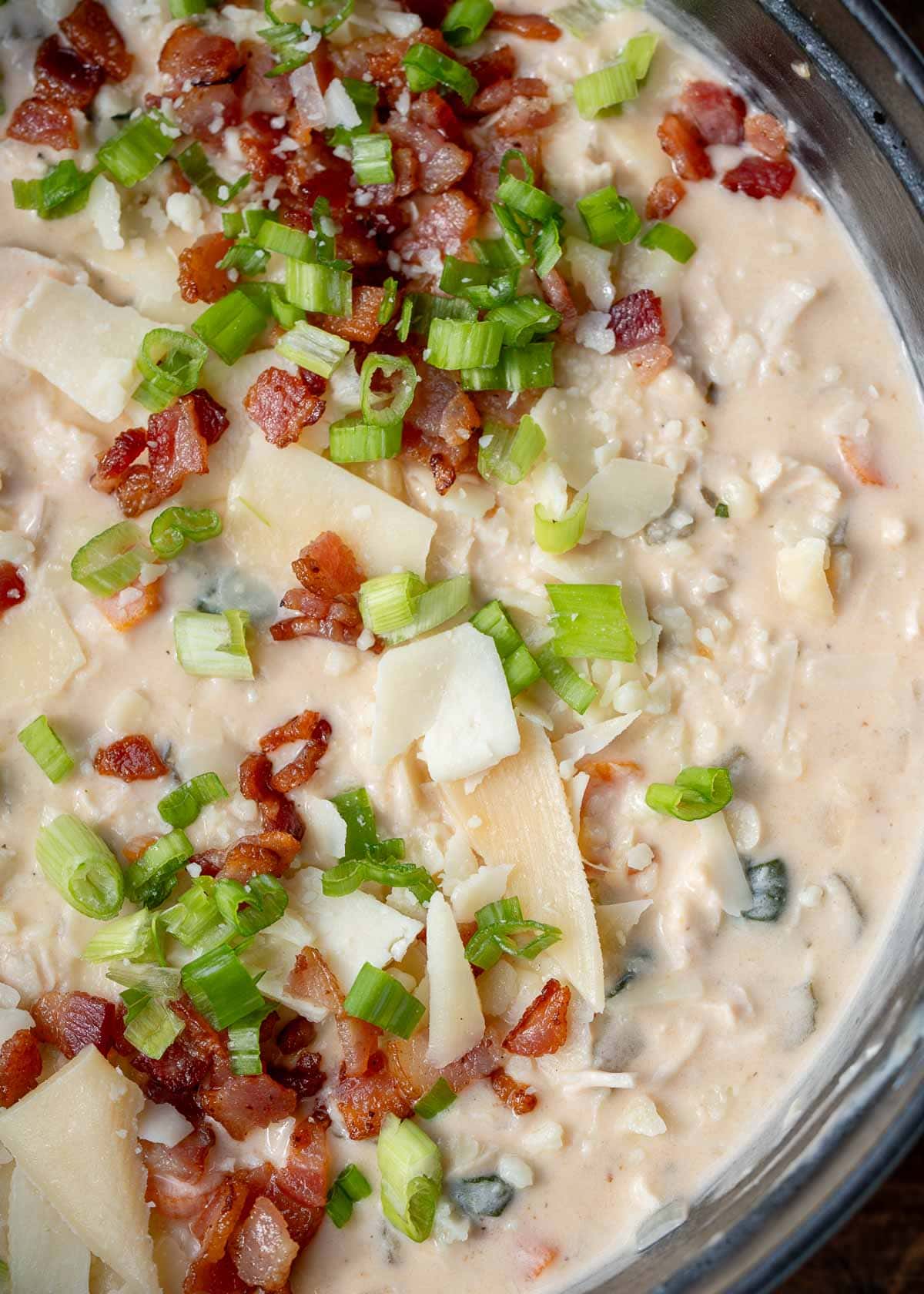 a large pot full of crack chicken soup topped with cheese, green onions, and crispy bacon