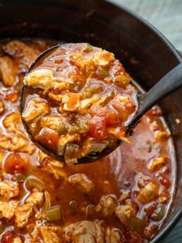 a ladle full of spicy chicken soup over a full dutch oven