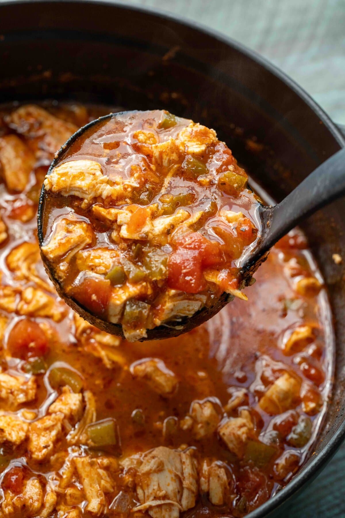 a ladle full of spicy chicken soup over a full dutch oven