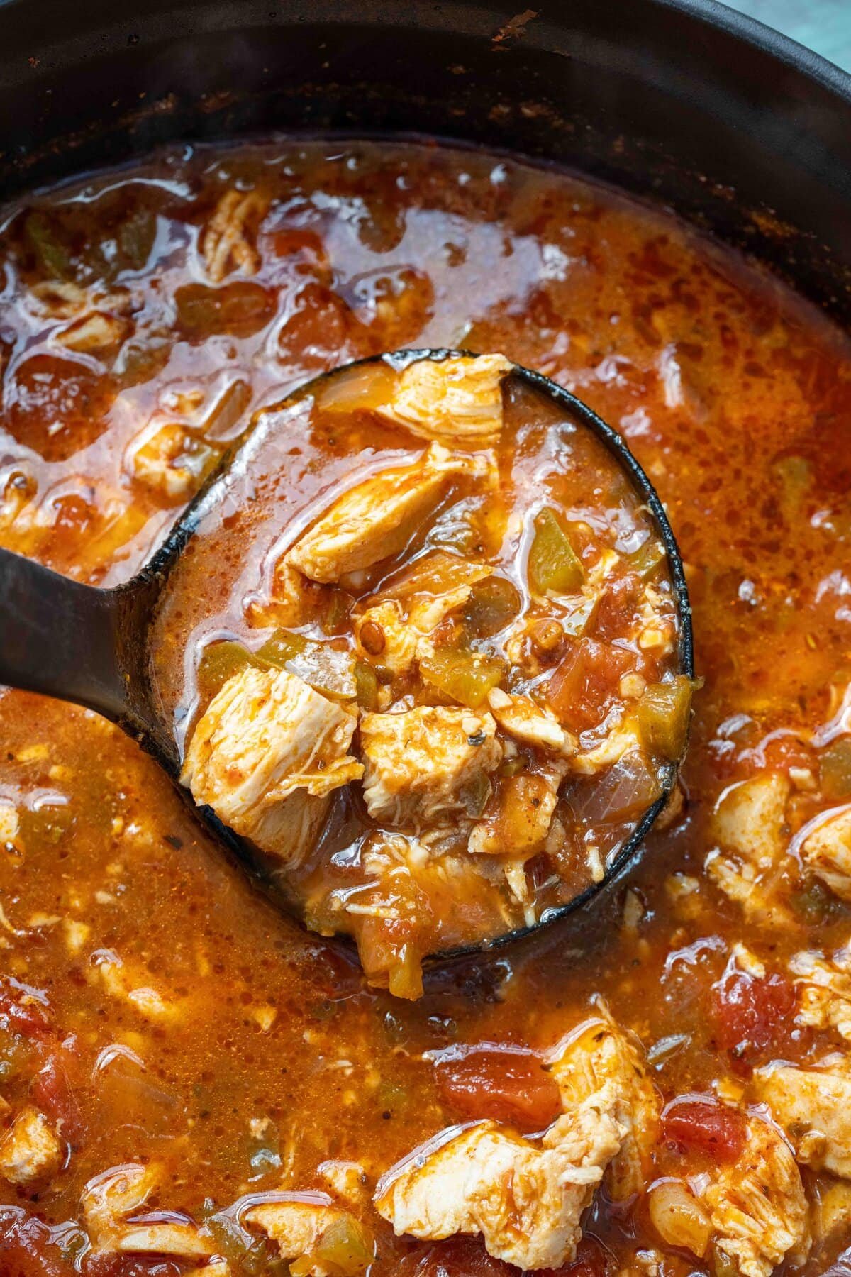 overhead shot showing a ladle full of spicy soup over a dutch oven full of chicken and pepper soup
