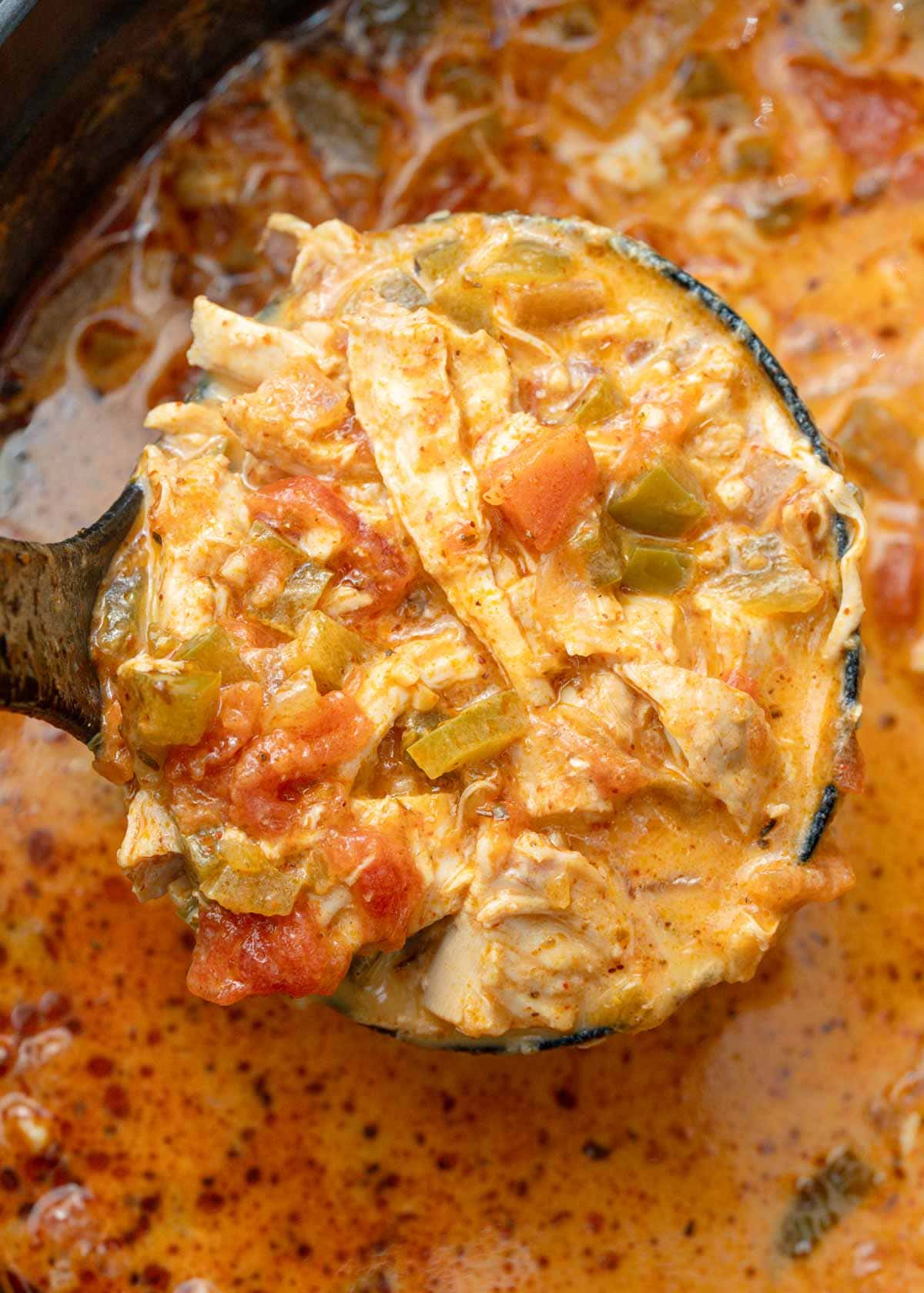 a large ladle full of chicken soup with peppers, tomatoes, and cheese