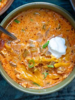 a closeup of a bowl full of creamy chipotle chicken soup garnished with extra cheese, a dollop of sour cream, and chopped green onions