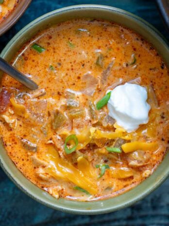 a closeup of a bowl full of creamy chipotle chicken soup garnished with extra cheese, a dollop of sour cream, and chopped green onions