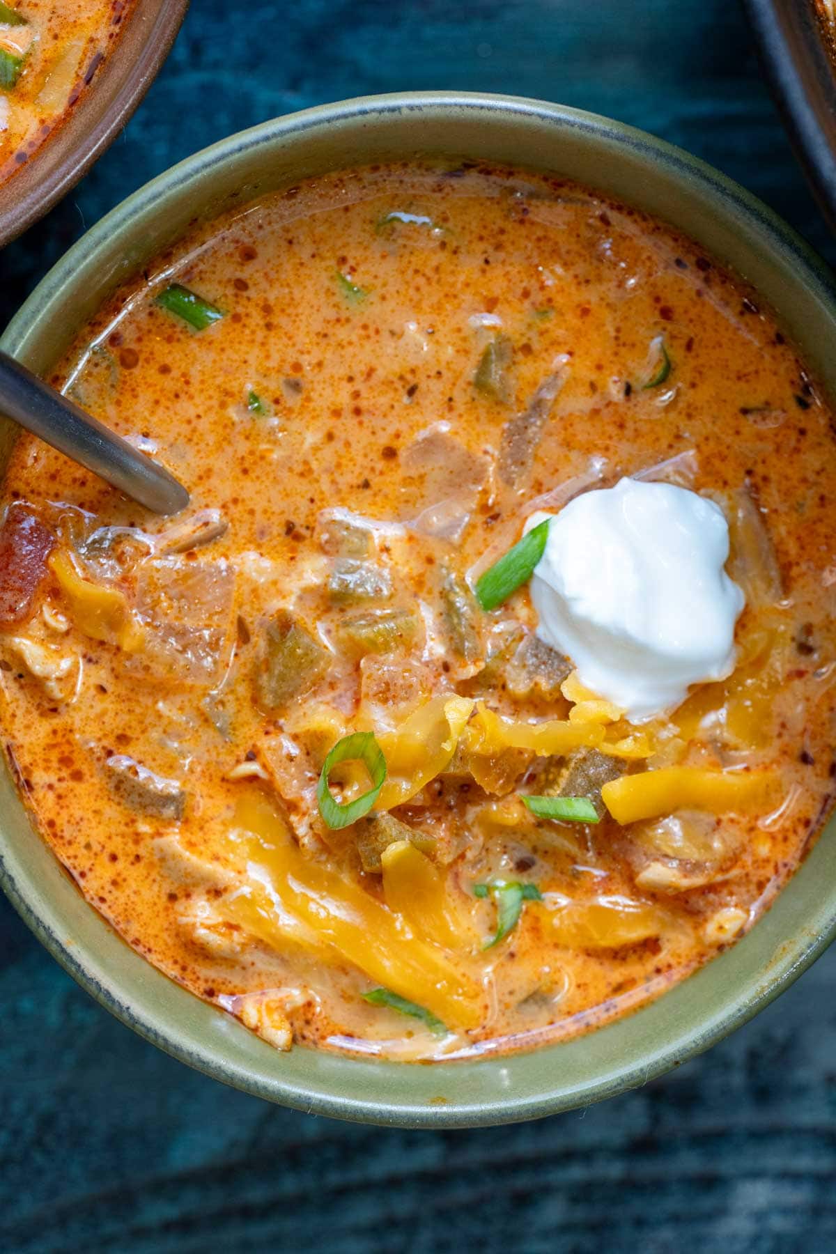 a closeup of a bowl full of creamy chipotle chicken soup garnished with extra cheese, a dollop of sour cream, and chopped green onions
