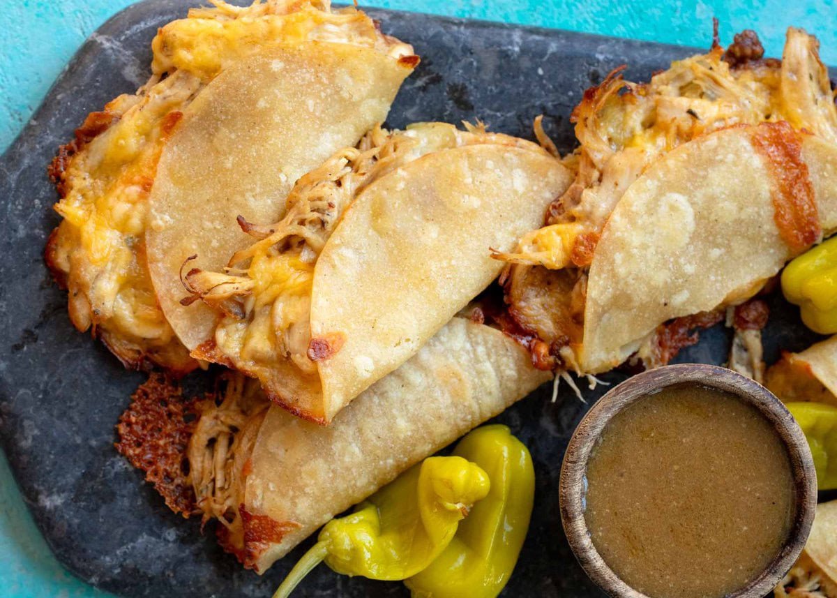 a platter topped with several baked mississippi chicken tacos with a side of pepperoncini and mississippi sauce