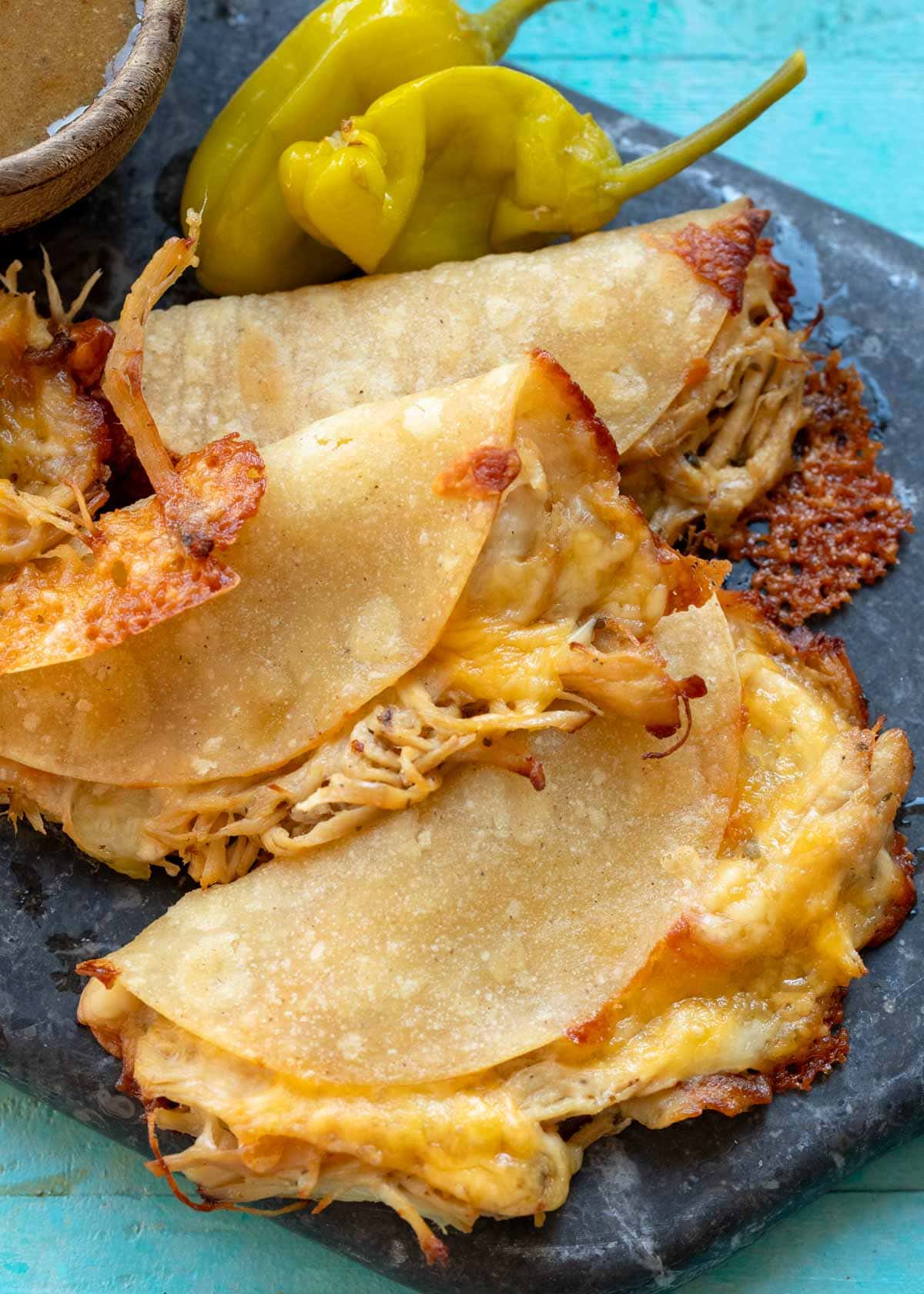 Three Mississippi Chicken Tacos piled on a plate with a side of pepperoncini and dipping sauce