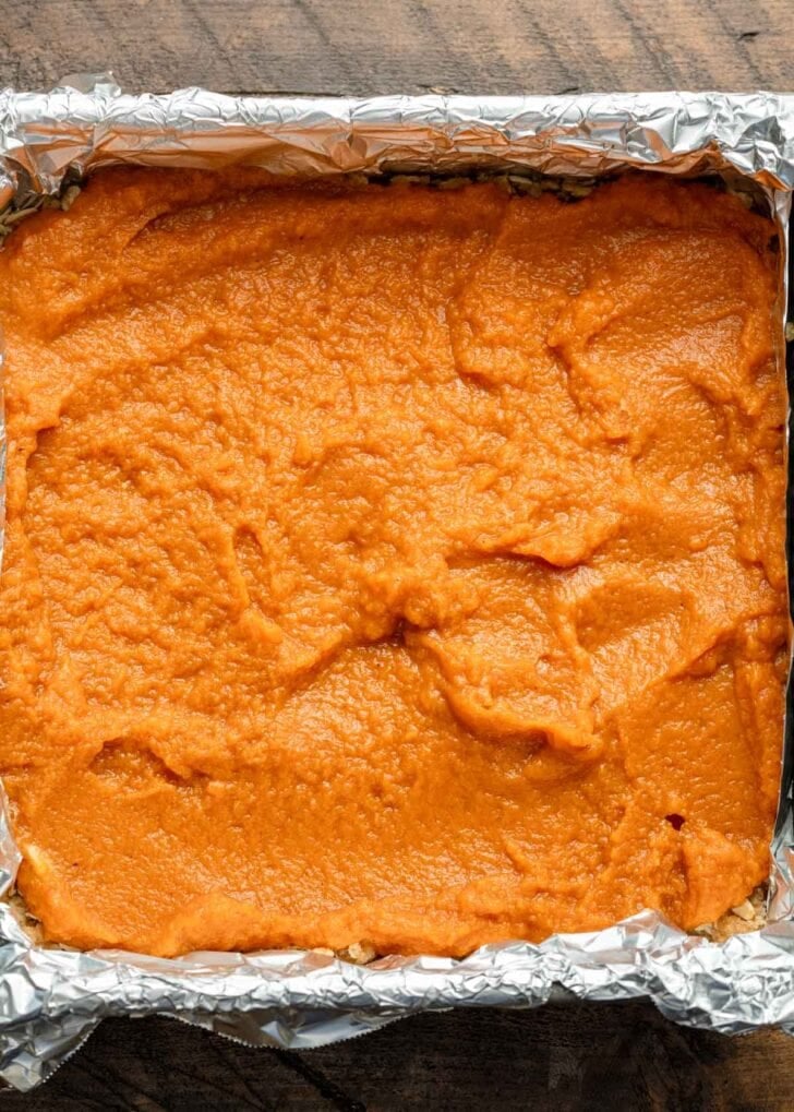 Pumpkin pie filling smoothed over an oat crust in a square baking dish