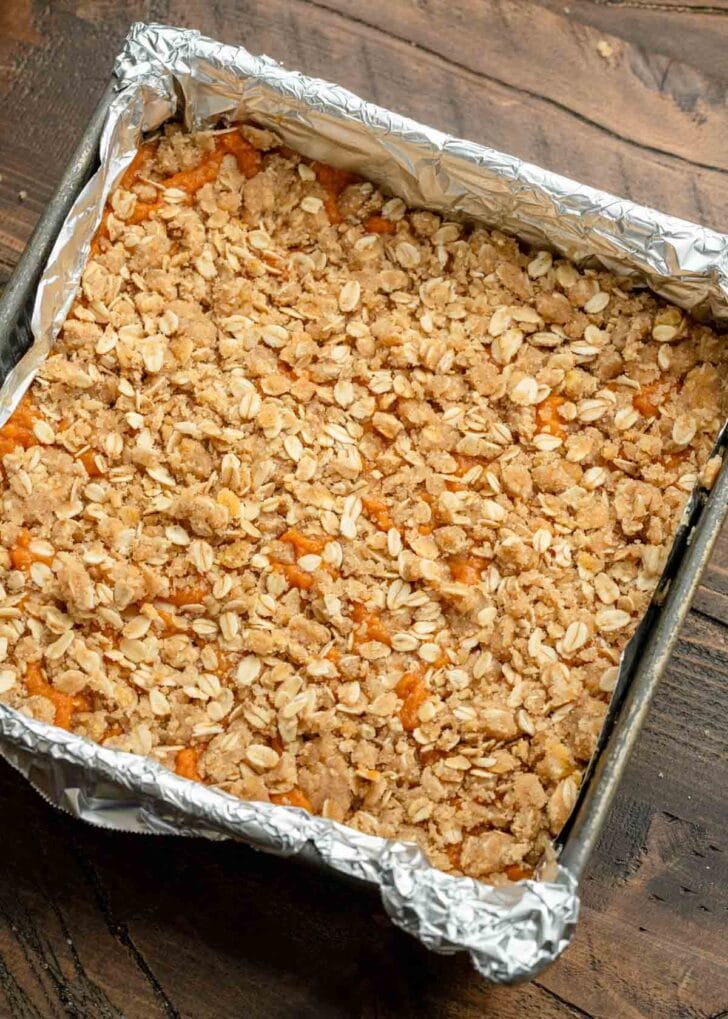 Oat crumble topping sprinkled over pumpkin pie filling in a baking dish
