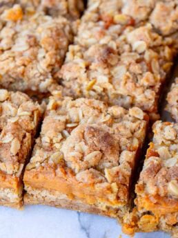 Pumpkin Bars sliced into squares, layered with pumpkin pie filling and oatmeal crumb topping.