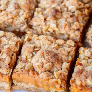 Pumpkin Bars sliced into squares, layered with pumpkin pie filling and oatmeal crumb topping.