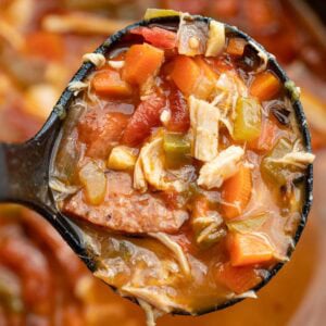 A ladle full of andouille sausage soup over a large pot