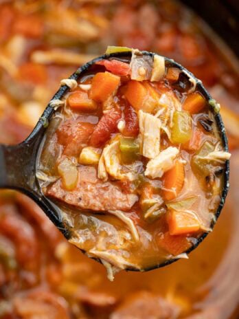 A ladle full of andouille sausage soup over a large pot
