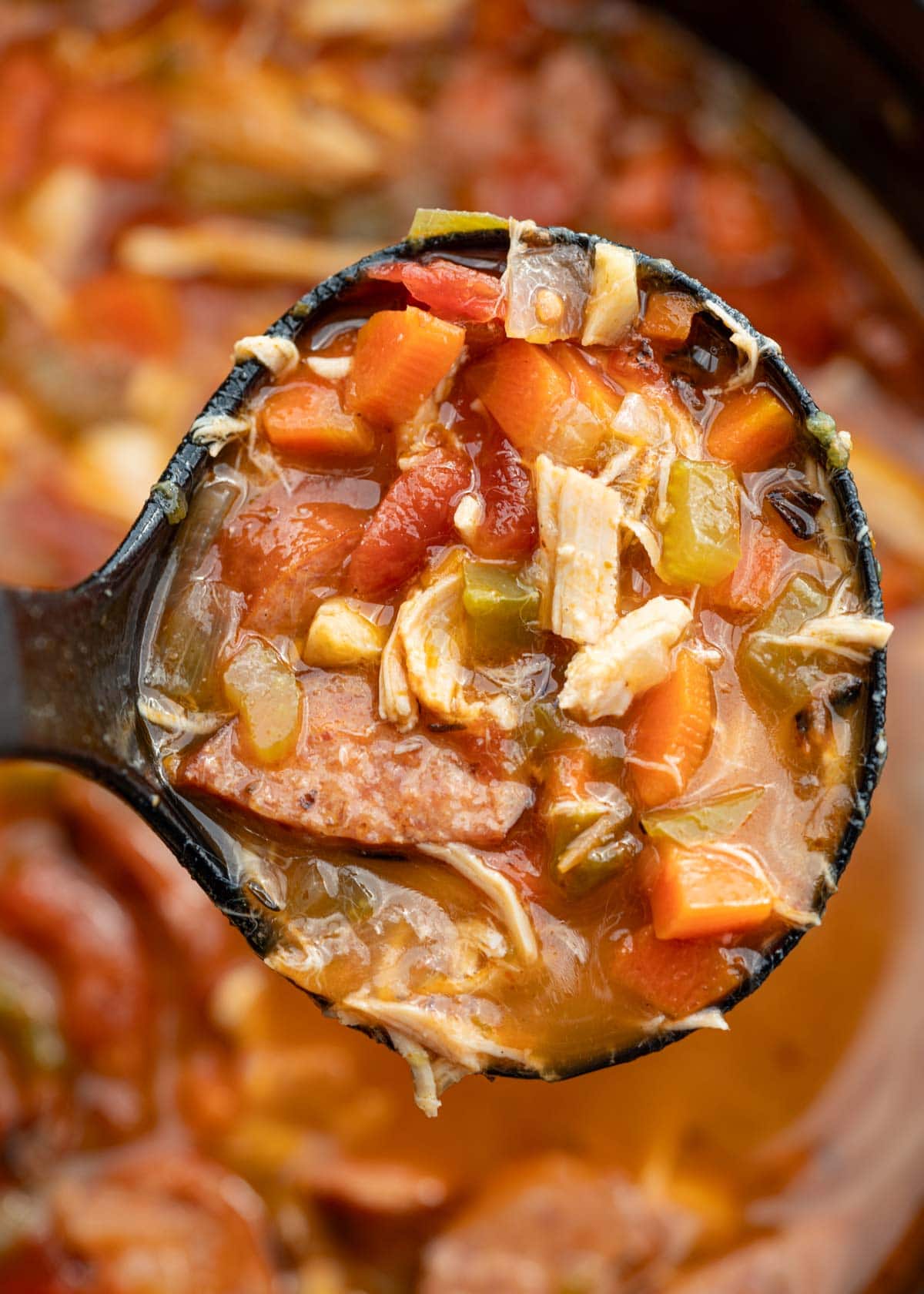 A ladle full of andouille sausage soup over a large pot