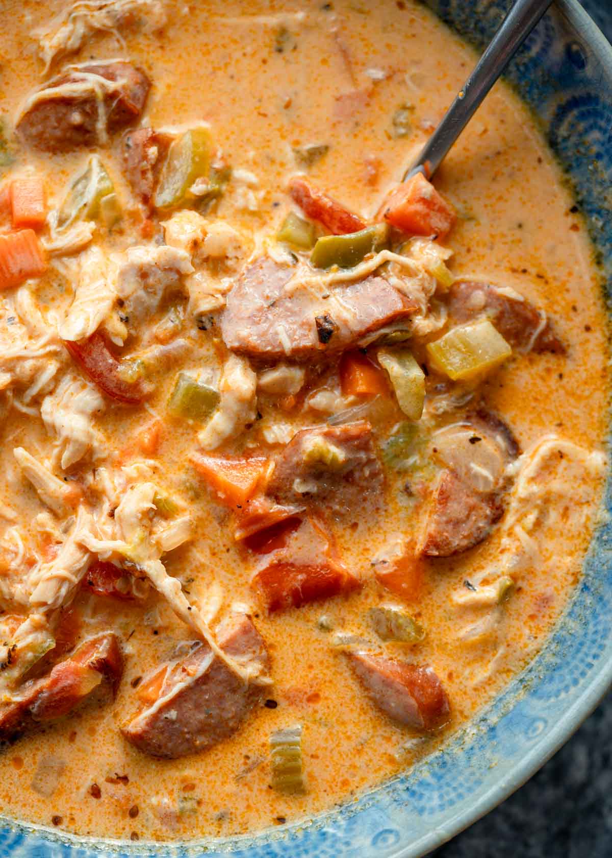 a big spoonful of cheesy Cajun chicken and sausage soup in a blue bowl