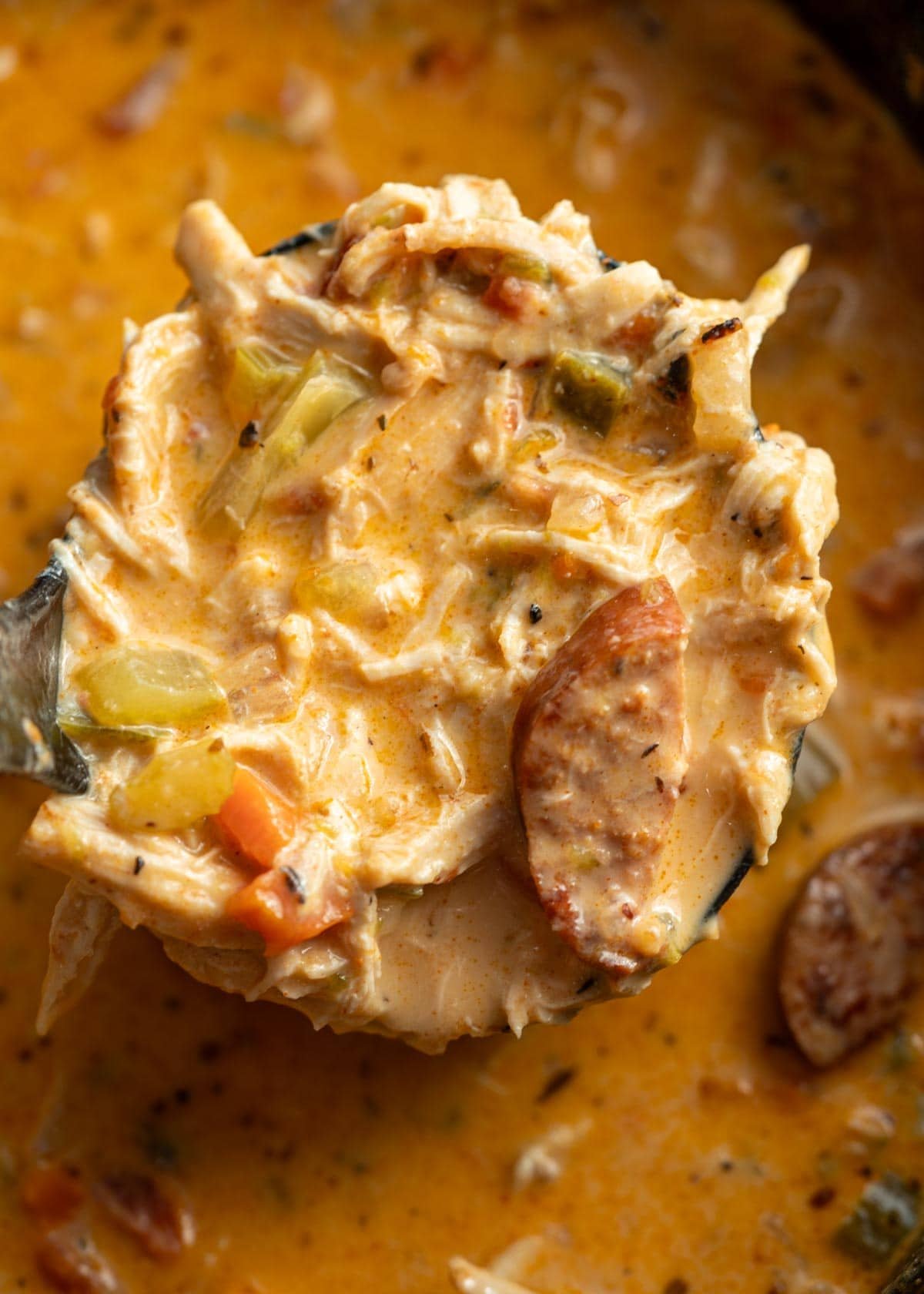 a large ladle full of creamy, cheesy cajun chicken sausage soup over a large pot