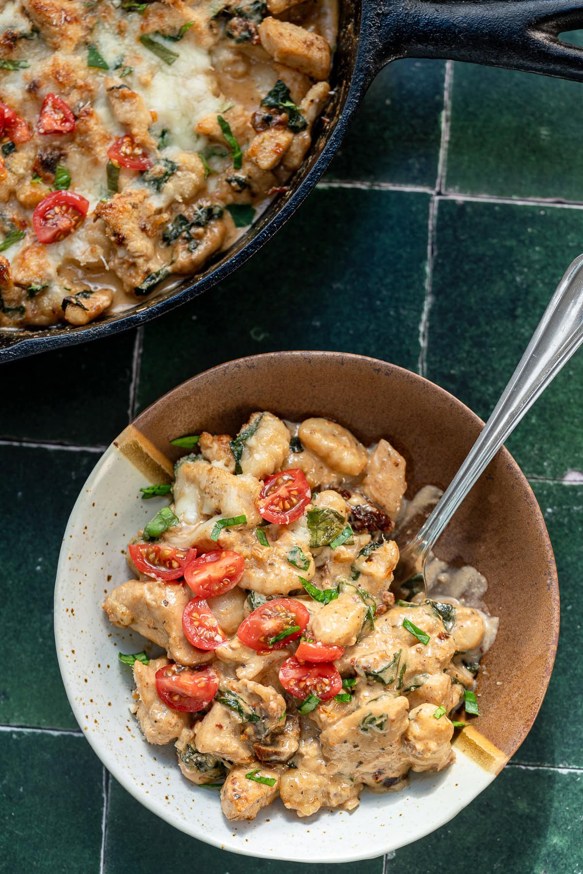 an overhead shot of marry me chicken gnocchi in a bowl with the larger skillet on the side.
