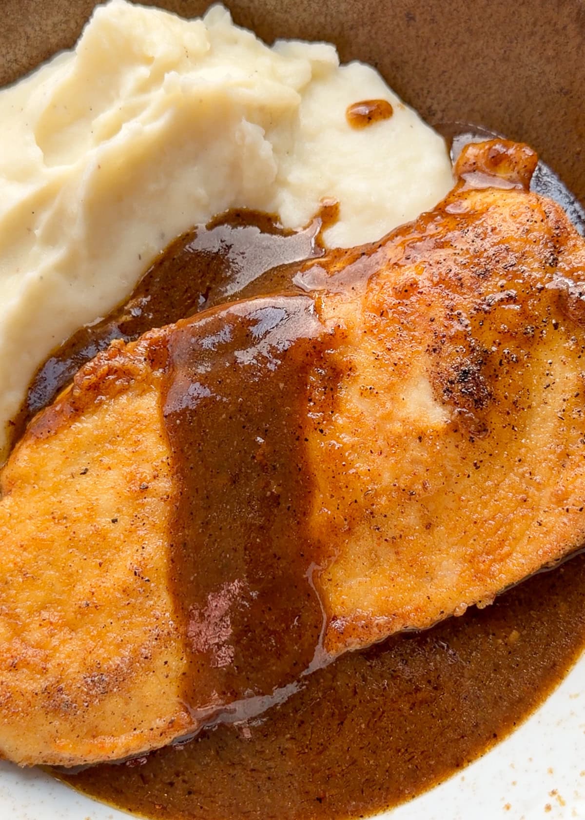 juicy chicken breast covered in gravy with a side of mashed potatoes