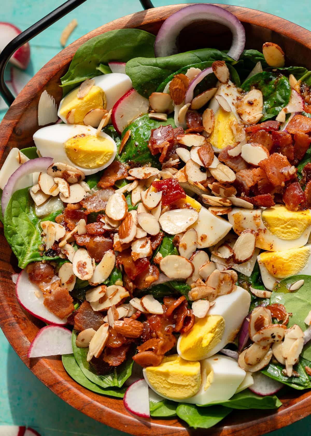 overhead shot showing almonds, bacon, hard boiled eggs, parmesan, radishes, and red onions over a bed of spinach