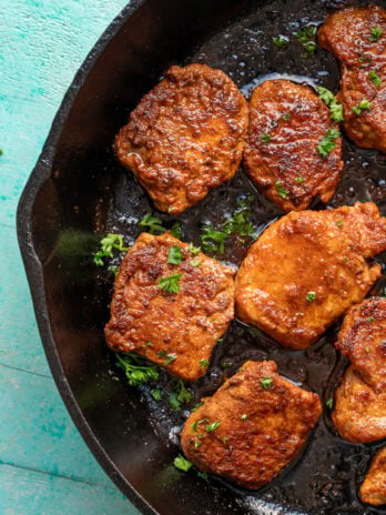 overhead image of pork medallions being garnished in cast iron skillet