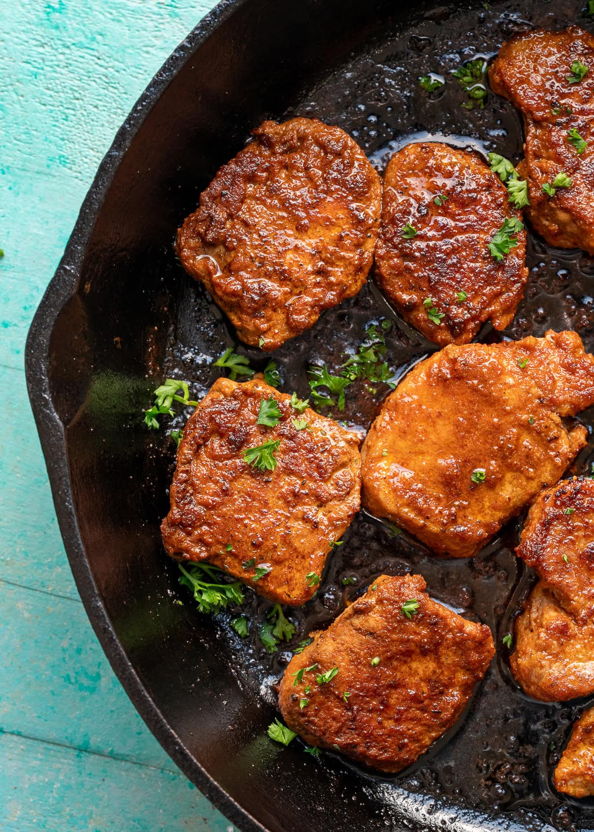 overhead image of pork medallions being garnished in cast iron skillet