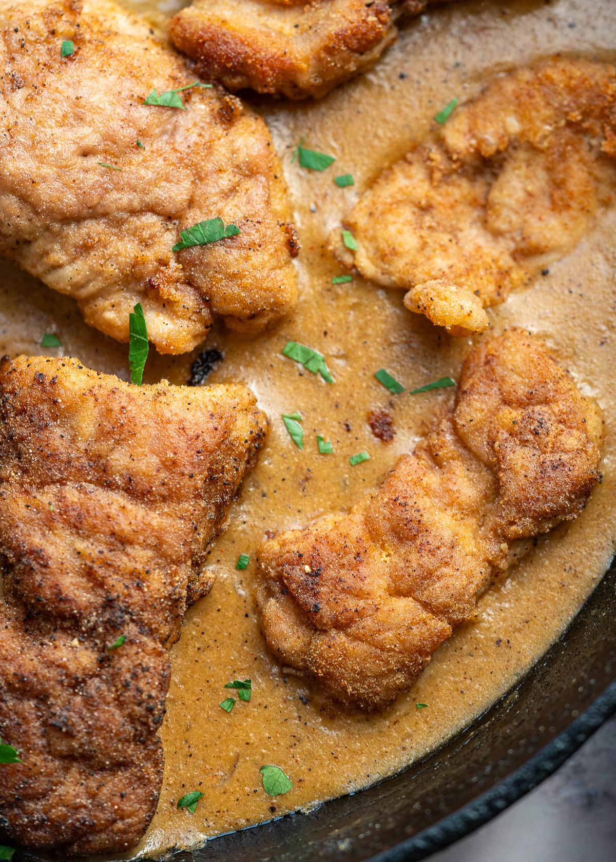 fresh herbs sprinkled on fried pork tenderloin in a creamy gravy