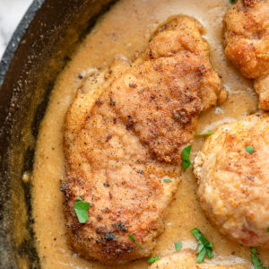 pieces of fried tenderloin in gravy garnished with fresh herbs