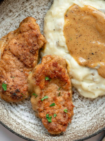 two pieces of fried pork tenderloin with a side of mashed potatoes and gravy