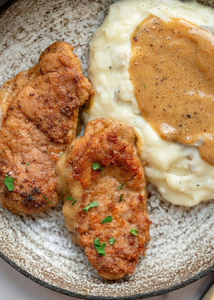 two pieces of fried pork tenderloin with a side of mashed potatoes and gravy
