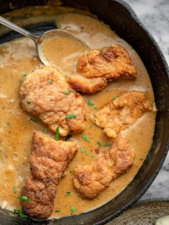 a spoon in the gravy surrounding fried pork tenderloin in a skillet
