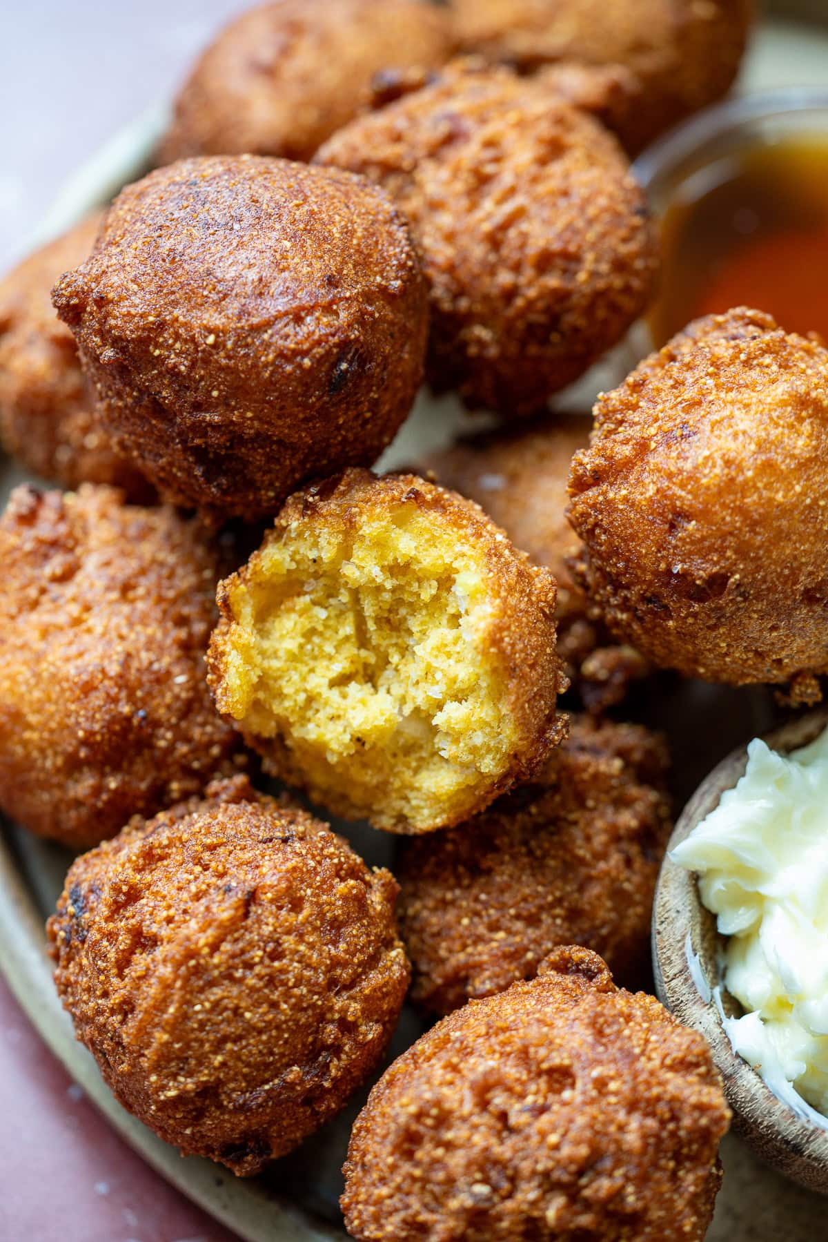 a platter of perfectly fried hush puppies; one is bitten and looks 