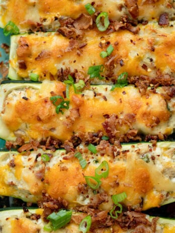 several chicken bacon ranch zucchini boats lined up garnished with green onions and bacon