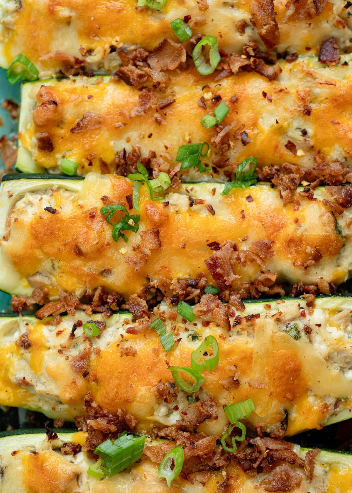 several chicken bacon ranch zucchini boats lined up garnished with green onions and bacon