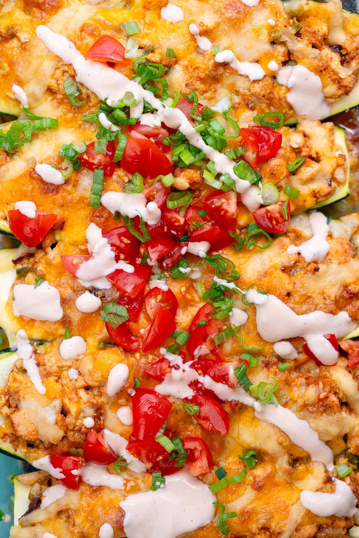 chipotle chicken stuffed zucchini boats topped with tomatoes, a creamy adobo sauce, and green onions