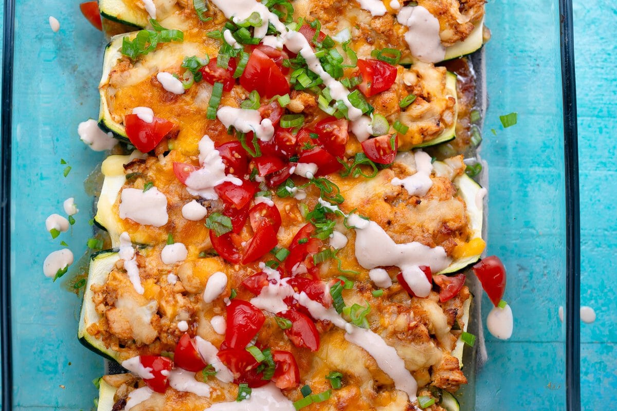 a baking dish full of chipotle chicken zucchini boats topped with sour cream, tomatoes, and green onions