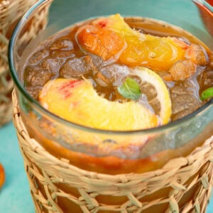 a glass full of peach tea, ice, lemon slices, peach slices, and mint leaves