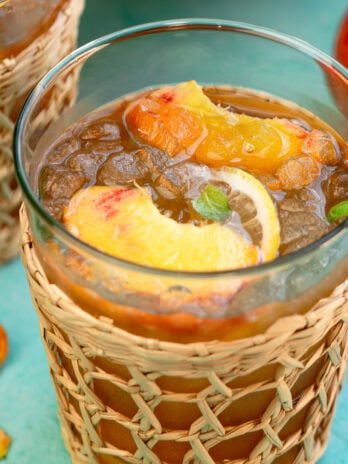 a glass full of peach tea, ice, lemon slices, peach slices, and mint leaves