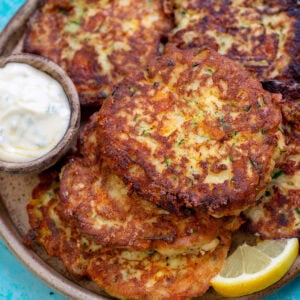 a platter full of crispy zucchini fritters with dipping sauce