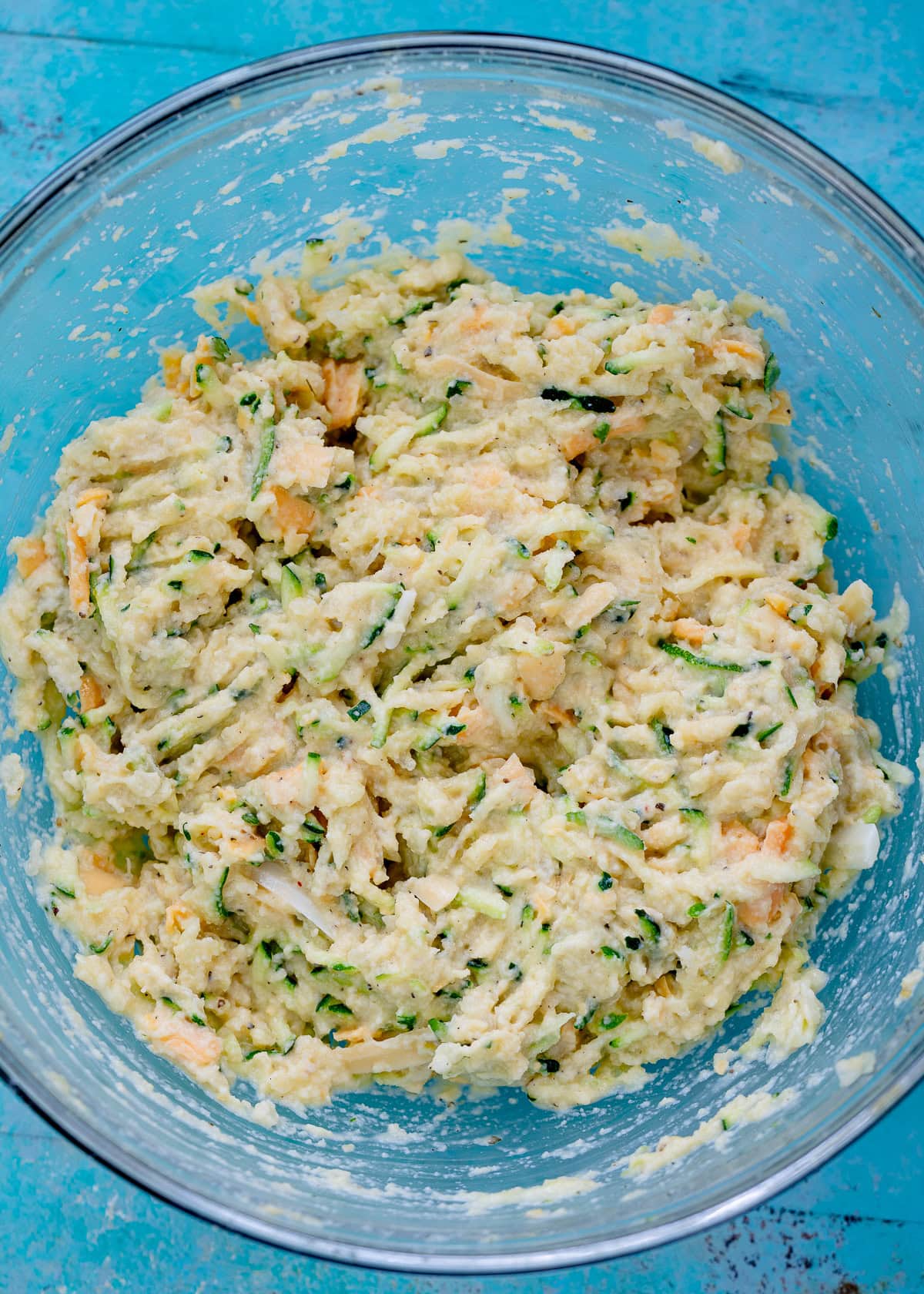 shredded zucchini mixed with eggs, coconut flour, onion, and seasonings in a glass bowl