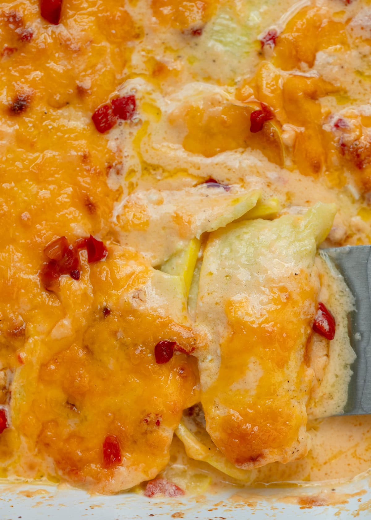 a metal spatula grabbing a serving of squash casserole in a casserole dish