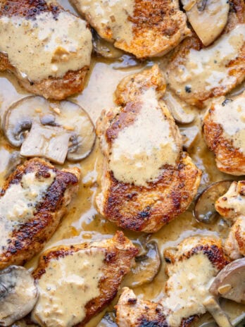 a skillet full of fried pork medallions with creamy mushroom sauce