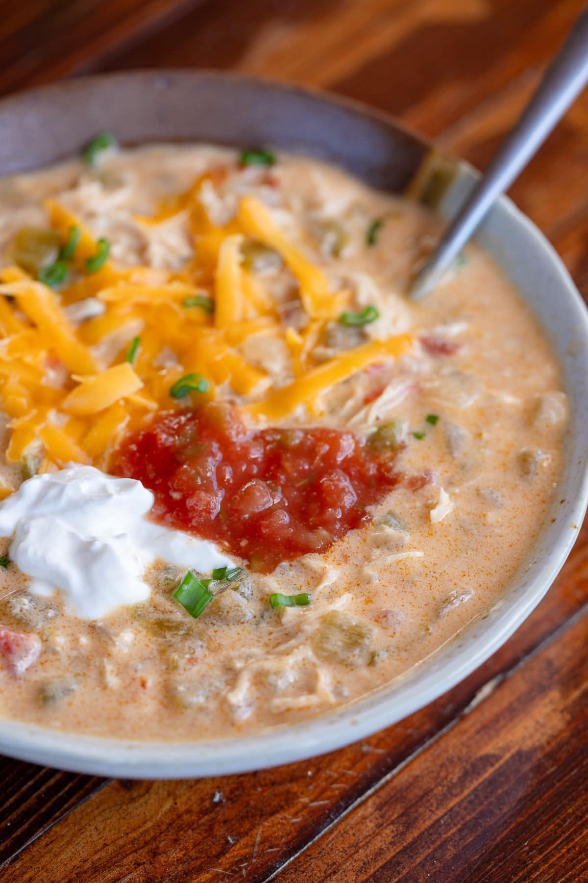 a bowl of chicken taco soup with sour cream, salsa, and cheese toppings