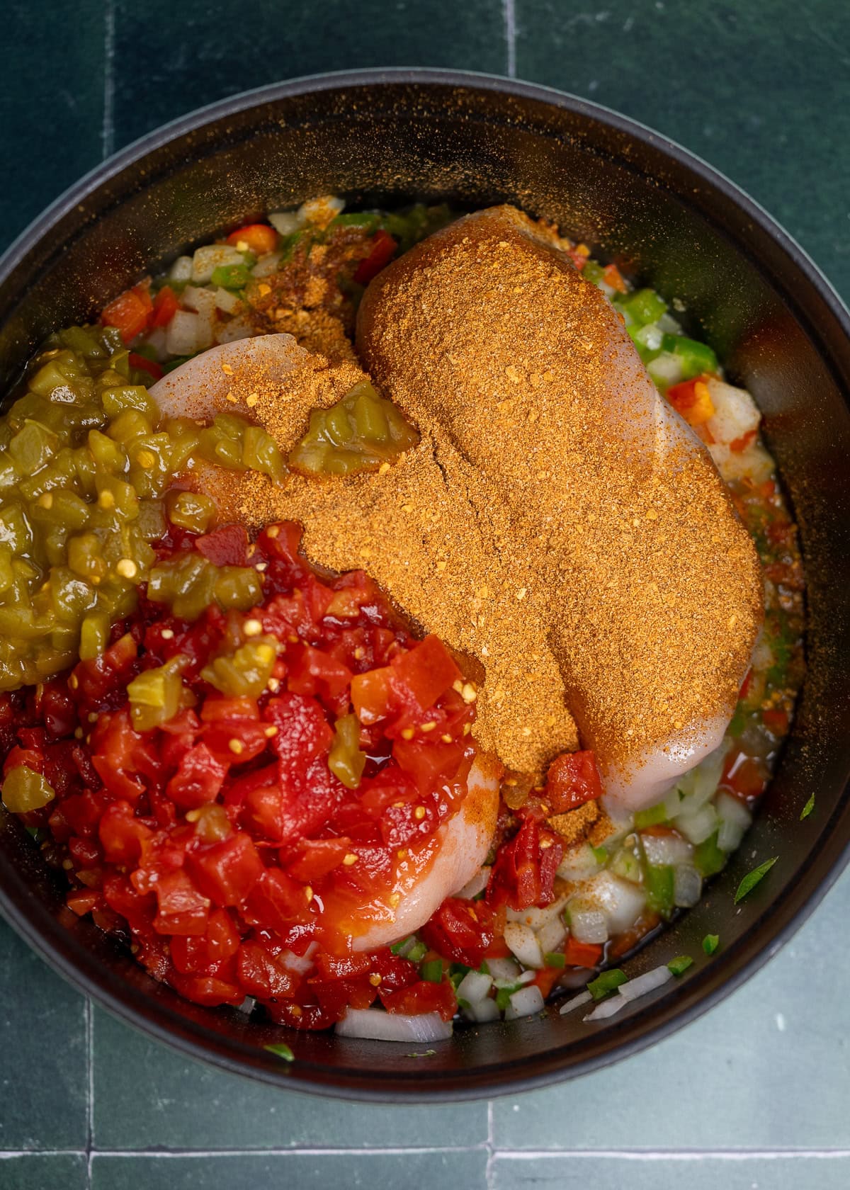 sauteed onion and peppers with chicken breasts, green chiles, rotel tomatoes, and taco seasoning in a pot